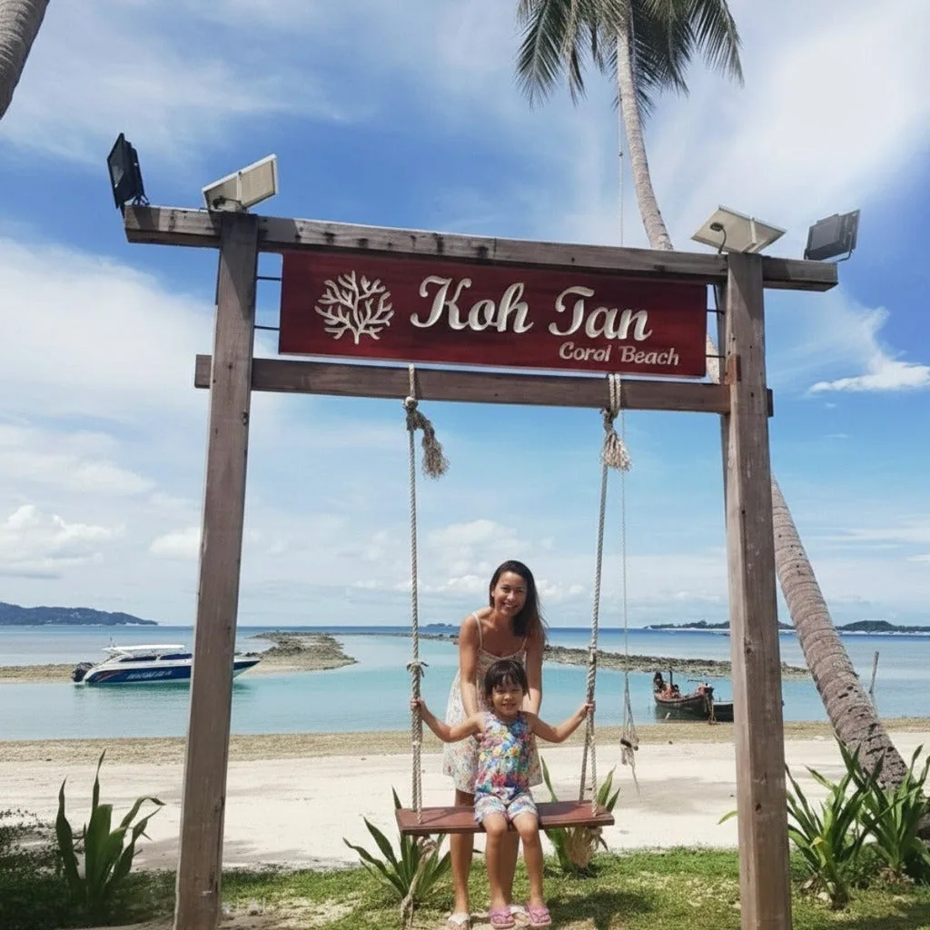 Mother and daughter on the swing under the Koh Tan Coral Beach sign, Koh Samui snorkeling stop